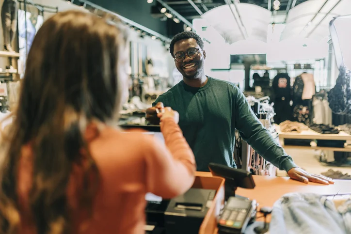 Clothing store owner handing a male customer a shopping bag with his clothing items. Happy small business owner assisting an online shopper during an in store collection